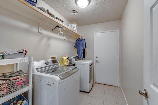 clothes washing area featuring washer and clothes dryer, light tile patterned floors, and a textured ceiling