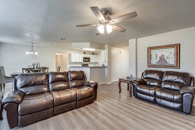 living room with ceiling fan with notable chandelier, sink, light wood-type flooring, and a textured ceiling