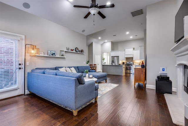 living room with ceiling fan, a high end fireplace, and dark wood-type flooring