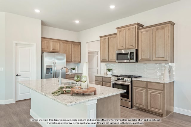 kitchen featuring appliances with stainless steel finishes, light stone counters, sink, a center island with sink, and light hardwood / wood-style flooring