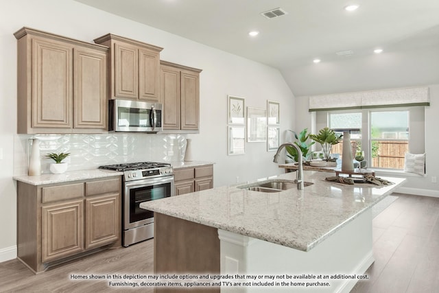 kitchen with stainless steel appliances, vaulted ceiling, a kitchen island with sink, sink, and light hardwood / wood-style flooring