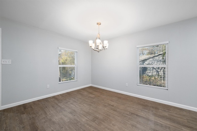 empty room with dark wood-type flooring and an inviting chandelier