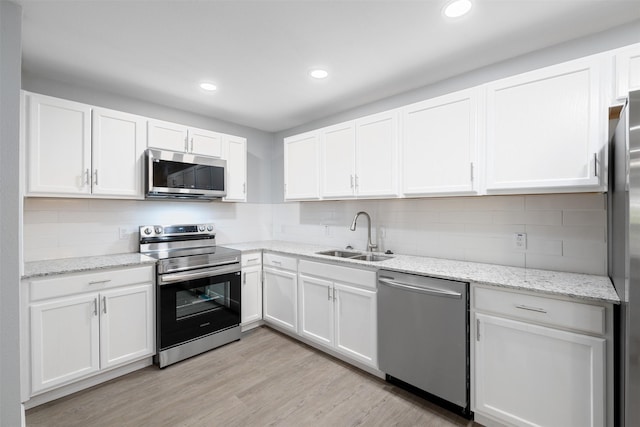 kitchen with light stone countertops, appliances with stainless steel finishes, sink, light hardwood / wood-style floors, and white cabinetry