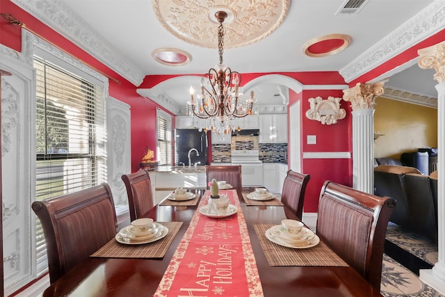 dining area with ornate columns, a notable chandelier, ornamental molding, and sink