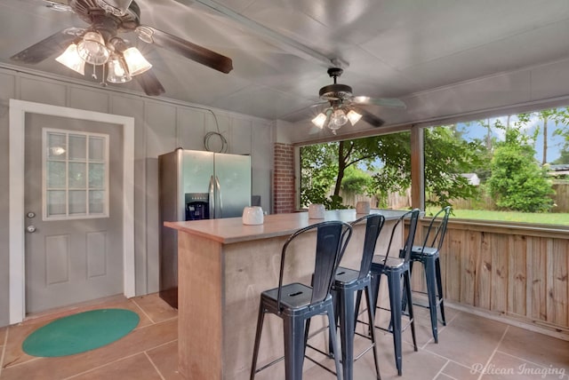 kitchen with light tile patterned floors, a breakfast bar area, ceiling fan, and stainless steel refrigerator with ice dispenser