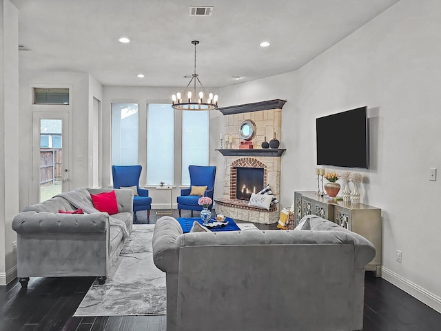 living room featuring dark hardwood / wood-style flooring, an inviting chandelier, and a stone fireplace