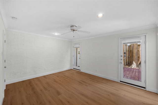 empty room featuring light hardwood / wood-style floors, ceiling fan, crown molding, and brick wall