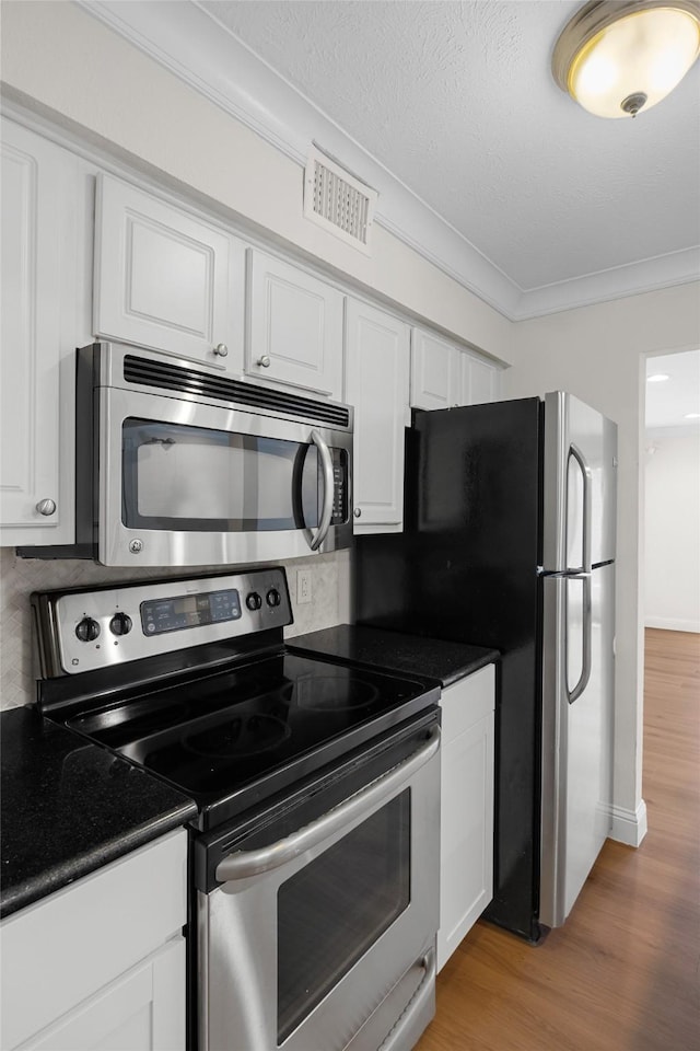 kitchen featuring hardwood / wood-style floors, white cabinets, stainless steel appliances, and ornamental molding