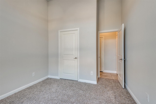 unfurnished bedroom featuring light carpet and a towering ceiling