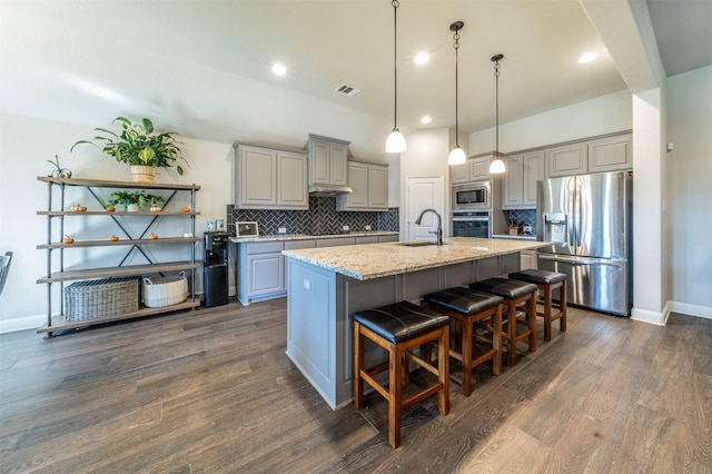 kitchen with appliances with stainless steel finishes, an island with sink, sink, gray cabinetry, and light stone counters