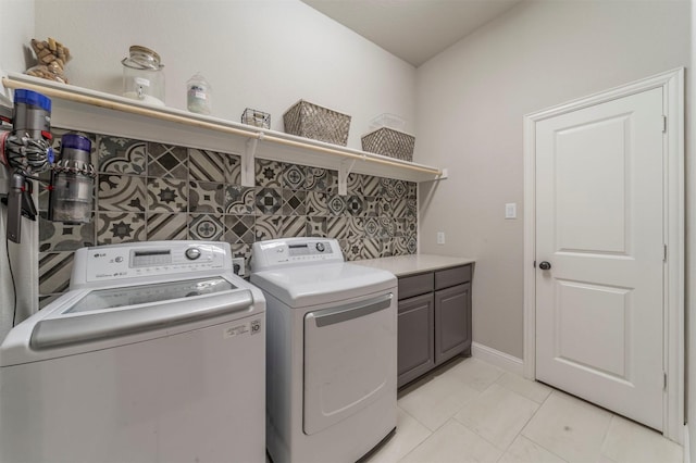 clothes washing area with cabinets, washing machine and clothes dryer, and light tile patterned floors