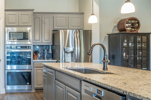 kitchen featuring gray cabinets, appliances with stainless steel finishes, sink, hanging light fixtures, and light stone countertops