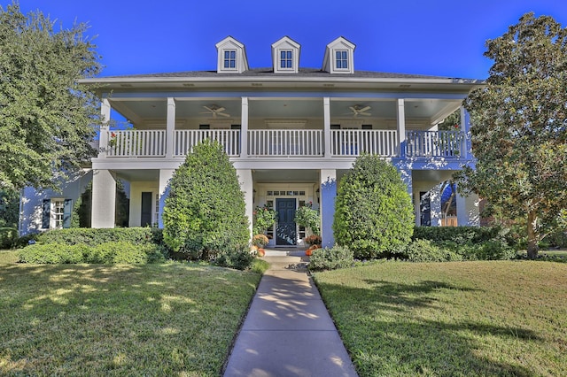 view of front facade with ceiling fan, a balcony, and a front lawn