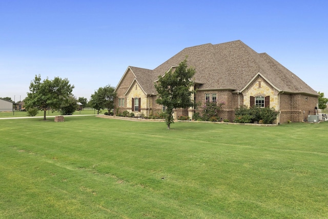 french country inspired facade featuring brick siding, central AC, a front lawn, and roof with shingles