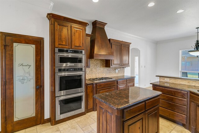 kitchen with tasteful backsplash, custom range hood, stainless steel appliances, crown molding, and dark stone countertops