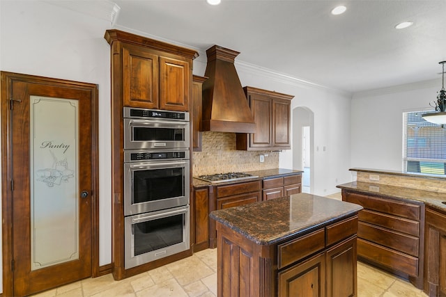 kitchen with arched walkways, custom range hood, appliances with stainless steel finishes, crown molding, and backsplash