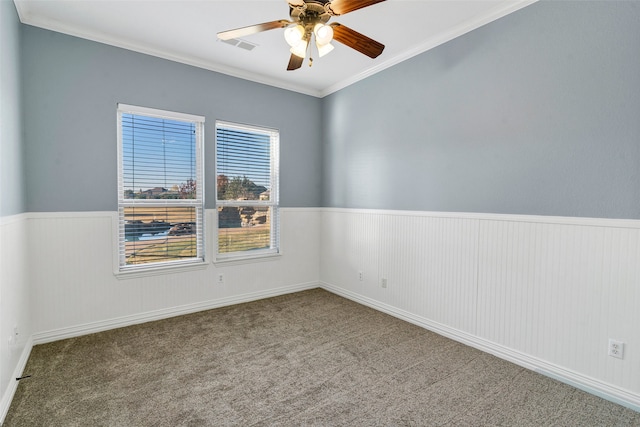 carpeted empty room featuring visible vents, ornamental molding, a ceiling fan, and wainscoting