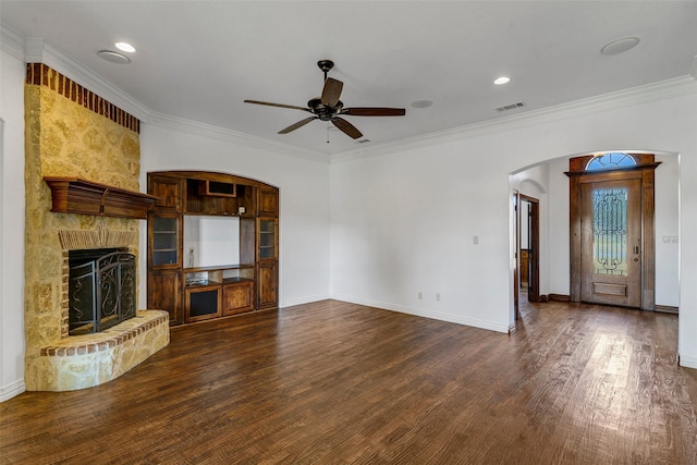 unfurnished living room featuring dark hardwood / wood-style floors, a stone fireplace, ceiling fan, and ornamental molding