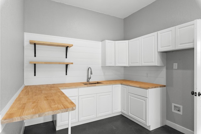 kitchen featuring baseboards, butcher block counters, white cabinetry, open shelves, and a sink