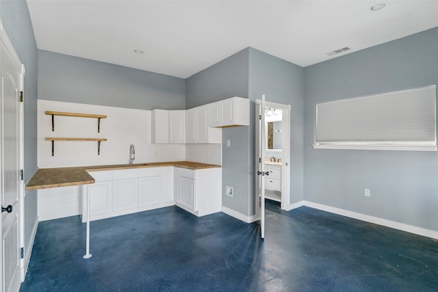 kitchen with concrete floors, a sink, visible vents, white cabinets, and open shelves