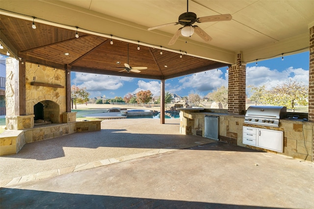 view of patio with an outdoor stone fireplace, a gazebo, an outdoor kitchen, a grill, and ceiling fan