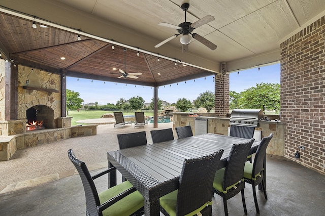 view of patio featuring an outdoor stone fireplace, ceiling fan, exterior kitchen, a pool, and grilling area