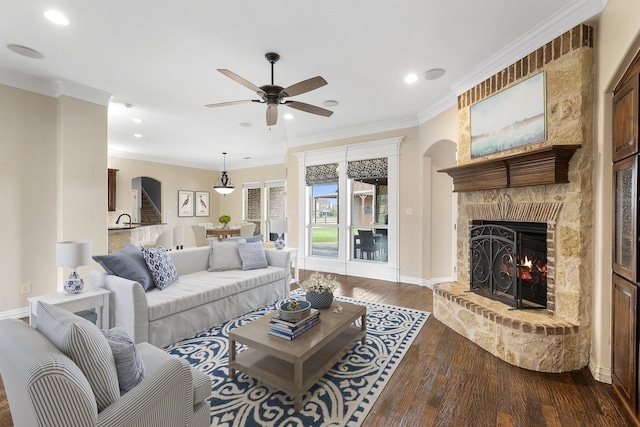 living room with dark hardwood / wood-style floors, a stone fireplace, ceiling fan, and ornamental molding