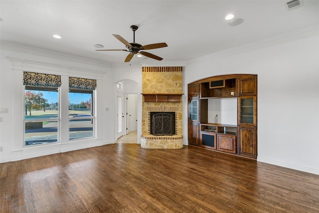 unfurnished living room with a stone fireplace, ornamental molding, wood finished floors, and a ceiling fan