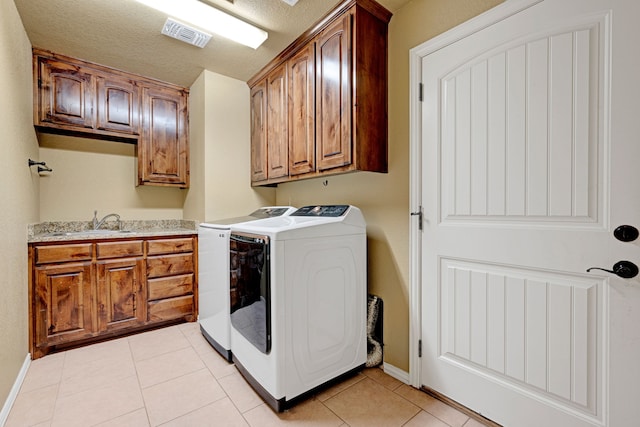 laundry room with cabinets, sink, light tile patterned floors, a textured ceiling, and washing machine and clothes dryer