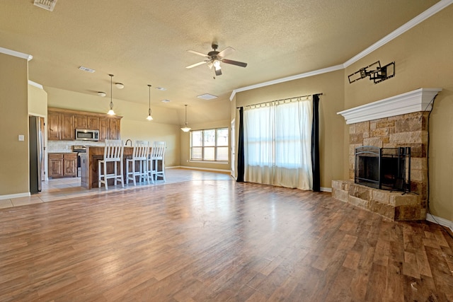 unfurnished living room with a stone fireplace, light hardwood / wood-style flooring, ceiling fan, ornamental molding, and a textured ceiling