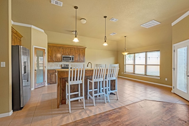 kitchen with a center island with sink, light hardwood / wood-style flooring, decorative backsplash, decorative light fixtures, and stainless steel appliances