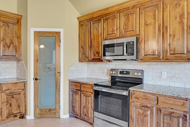 kitchen featuring backsplash, light stone countertops, light tile patterned floors, and stainless steel appliances