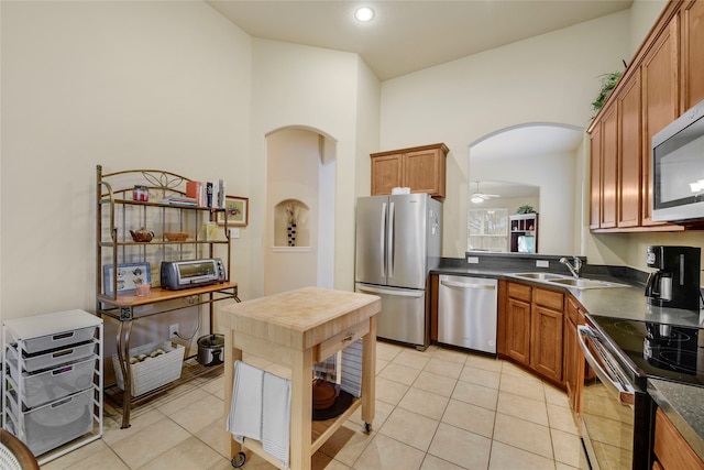 kitchen with sink, ceiling fan, a towering ceiling, light tile patterned flooring, and stainless steel appliances