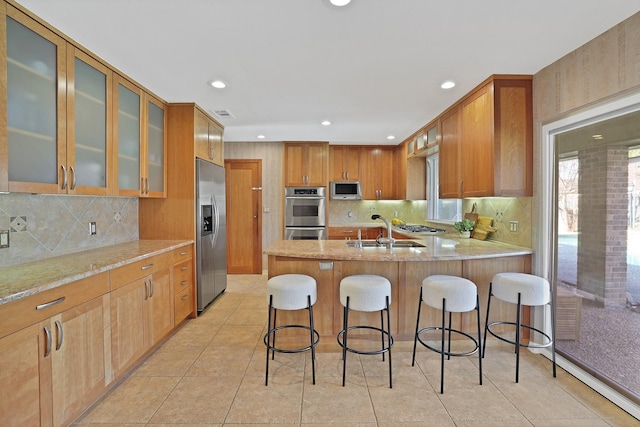 kitchen featuring light stone countertops, sink, a kitchen breakfast bar, light tile patterned floors, and appliances with stainless steel finishes