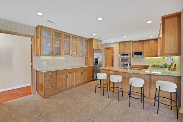 kitchen featuring kitchen peninsula, tasteful backsplash, a breakfast bar, stainless steel appliances, and sink