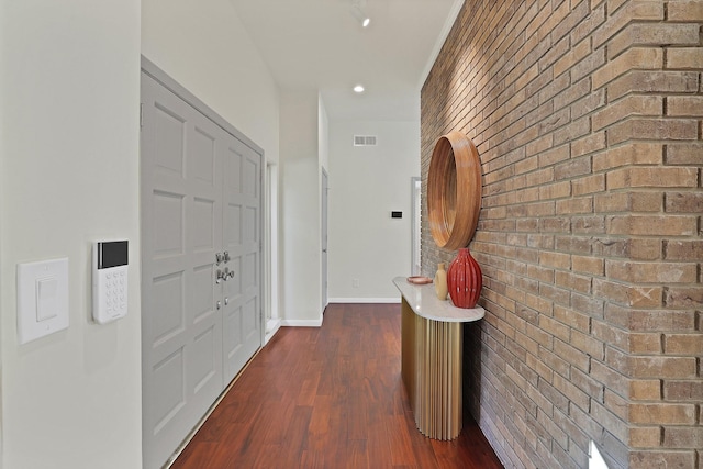 hallway featuring dark hardwood / wood-style flooring and brick wall