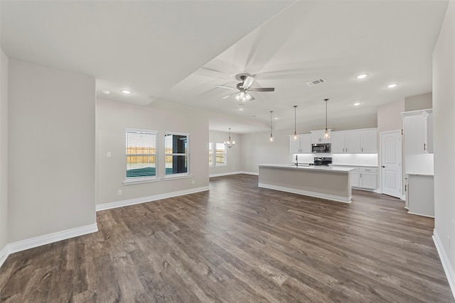 unfurnished living room featuring ceiling fan with notable chandelier, sink, and dark wood-type flooring