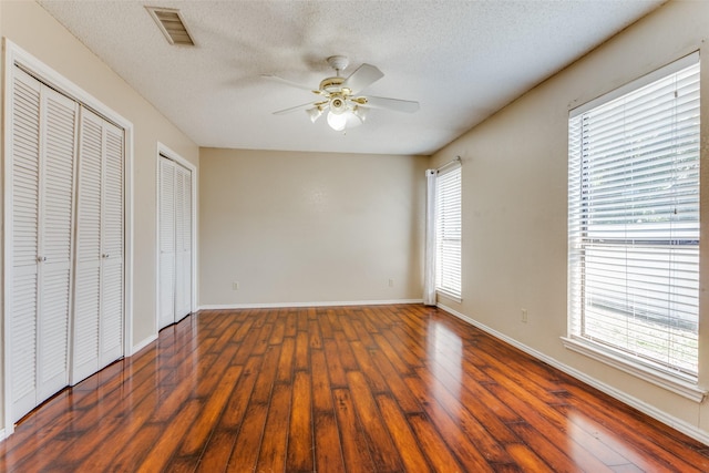 unfurnished bedroom featuring dark wood-type flooring, ceiling fan, a textured ceiling, and two closets