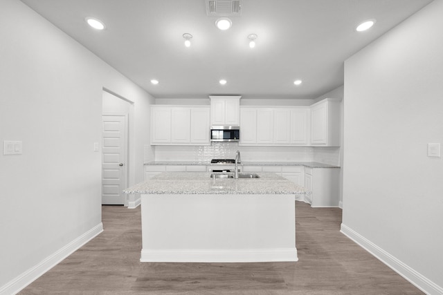 kitchen with sink, decorative backsplash, an island with sink, light stone counters, and white cabinetry