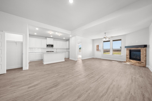 unfurnished living room featuring light wood-type flooring, a brick fireplace, and ceiling fan