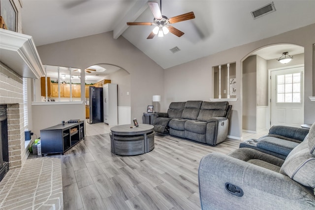 living room featuring ceiling fan, hardwood / wood-style floors, lofted ceiling with beams, and a brick fireplace