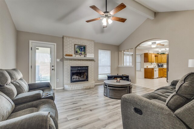 living room featuring a brick fireplace, ceiling fan, lofted ceiling with beams, and light wood-type flooring