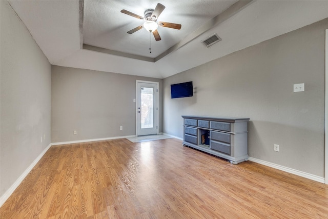 unfurnished living room with a tray ceiling, ceiling fan, a textured ceiling, and light wood-type flooring