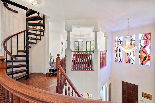 stairs featuring hardwood / wood-style floors, decorative columns, and a notable chandelier