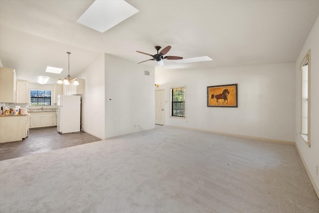 unfurnished living room with vaulted ceiling with skylight, ceiling fan with notable chandelier, and carpet