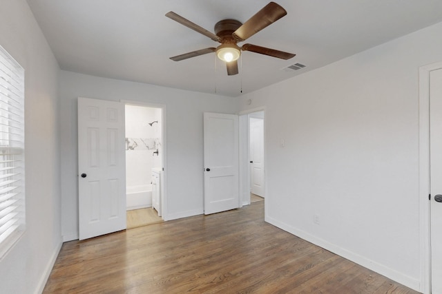 unfurnished bedroom with multiple windows, ensuite bathroom, hardwood / wood-style floors, and ceiling fan