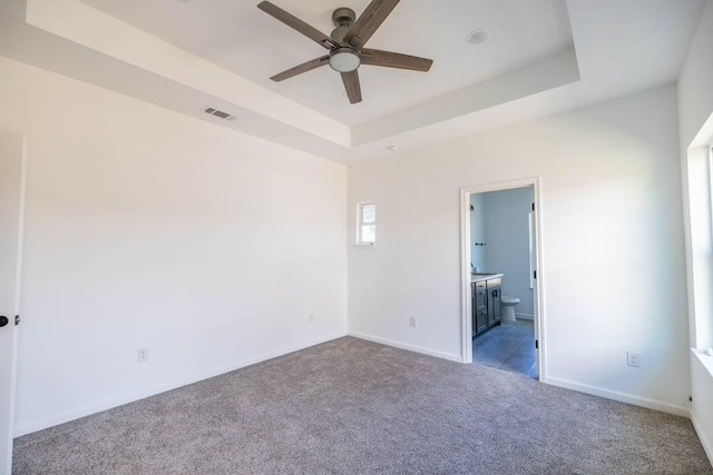 unfurnished bedroom with a raised ceiling, ensuite bathroom, ceiling fan, and light carpet