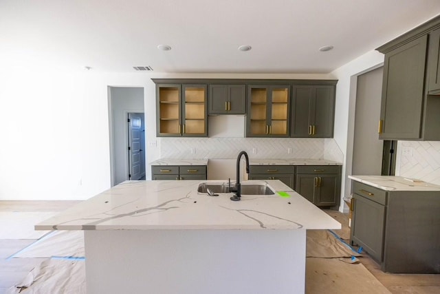 kitchen featuring decorative backsplash, light stone countertops, sink, and a kitchen island with sink