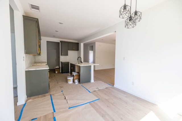 kitchen featuring sink, hanging light fixtures, a kitchen island with sink, decorative backsplash, and light wood-type flooring