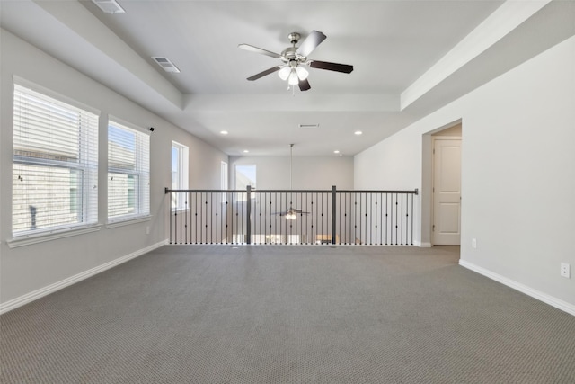 spare room with a tray ceiling, dark carpet, and ceiling fan